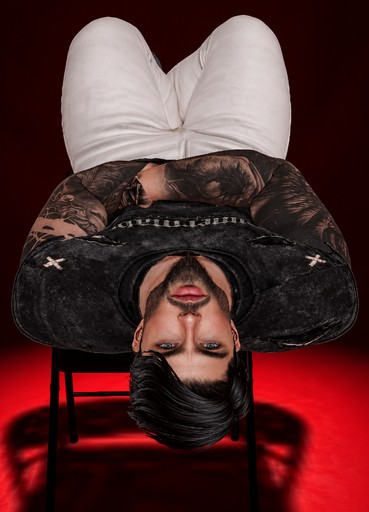 Upside-down person in dark clothing against a red background, surreal fashion photograph